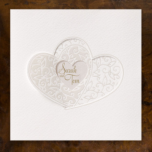 Vergrößerte Abbildung der Einladungskarte Weiße Hochzeitseinladungen mit zwei verschlungenen Herzen, die auch als Verschluss für die Karte dienen. Verziert mit stilisierten Blumenranken.