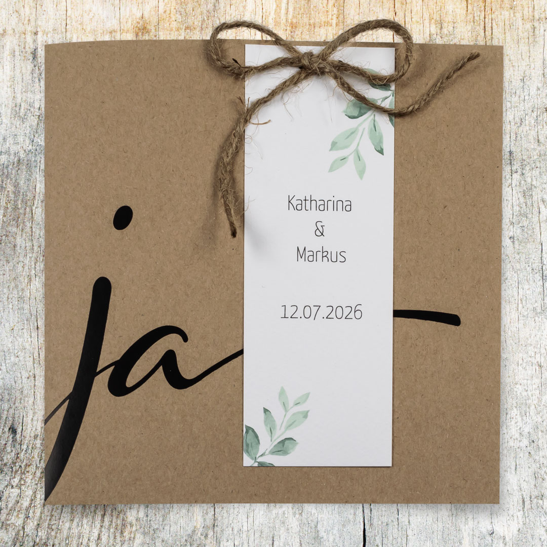 Vergrößerte Abbildung Vintage-Hochzeitseinladung aus braunem Kraftkarton, aufgedrucktem großen JA und weißen Anhängern.