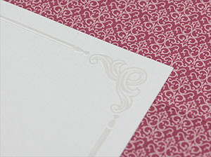 Detail der Prägung – vergrößerte Abbildung Elegant geprägte Hochzeitseinladung vor rotem Hintergrund.