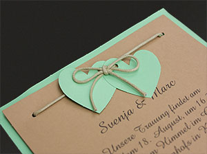 Detail 2 – vergrößerte Abbildung Zwei grüne Herzen, an eine Kordel geknüpft im Hintergrund brauner und grüner Karton.