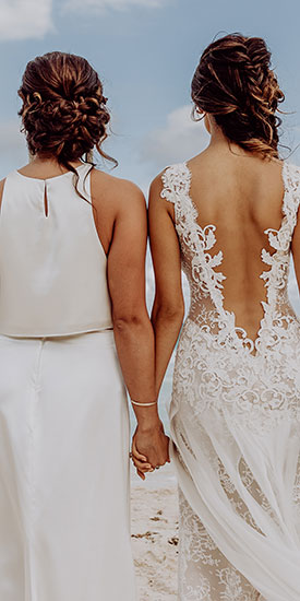 Regenbogenhochzeit. Braut und Braut Hand in Hand am Strand